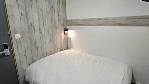 Una habitación con cama, puerta y una lámpara fijada a la pared.