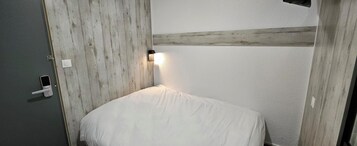 Una habitación con cama, puerta y una lámpara fijada a la pared.