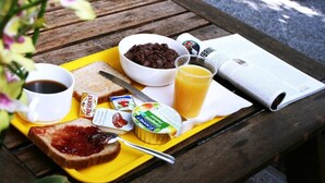 Una bandeja de desayuno con tostadas, mermelada, crema de chocolate, yogur, café y jugo de naranja sobre una mesa de madera.