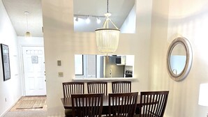 Un comedor con una araña, una cocina al fondo y un sillón redondo acolchado en primer plano.