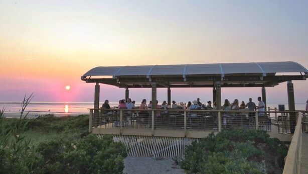 Un espacio de estar al aire libre con techo y vistas a la puesta de sol sobre el agua.