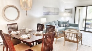 Un comedor con una mesa de madera dispuesta para cuatro personas, rodeada de sillas de madera. Se observan un espejo grande y una lámpara de araña en las paredes.