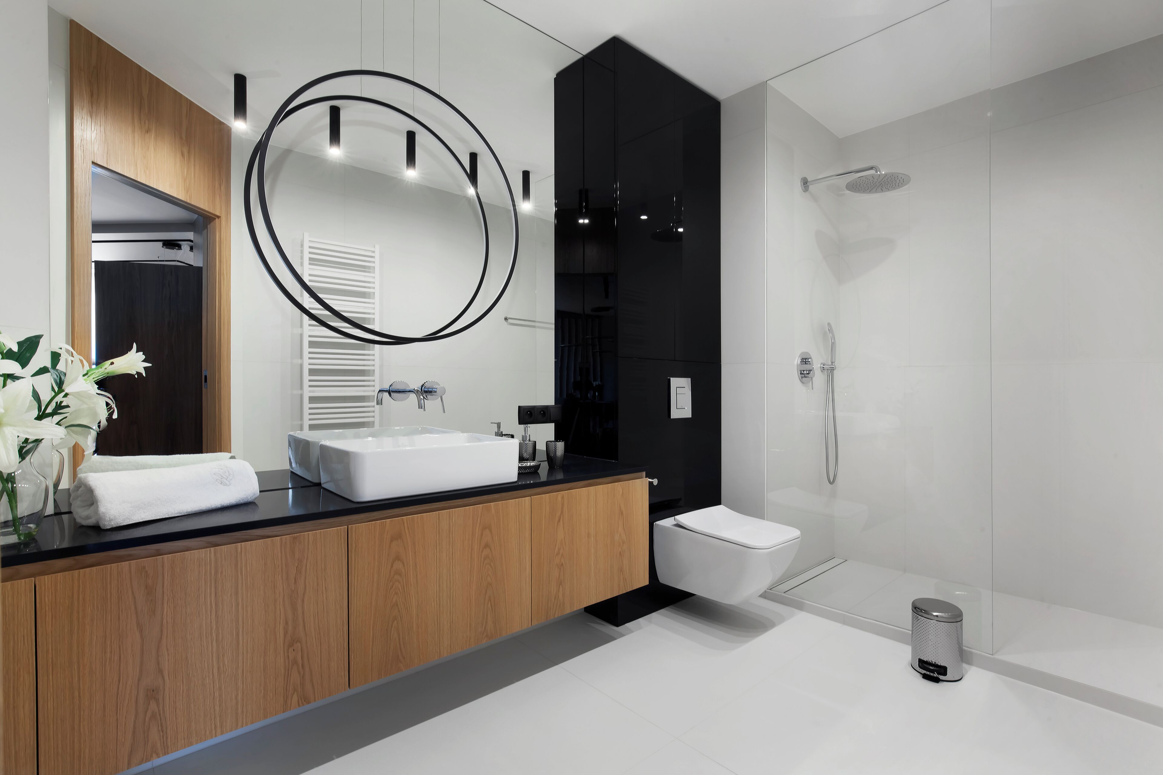 Un bagno moderno con un mobile bagno in legno, uno specchio grande, un lavandino bianco, un water e una cabina doccia in vetro.
