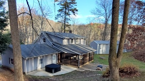 A two-story house with a covered porch and a small deck, surrounded by trees and a grassy yard.