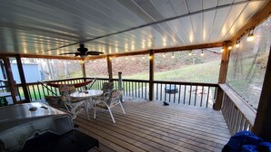 A covered outdoor deck with a table and chairs, a grill, and string lights.