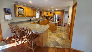 A kitchen with wooden cabinets, a granite countertop, a stainless steel refrigerator, and a central island with bar stools.
