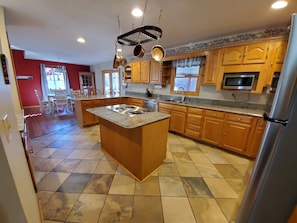 A kitchen with wooden cabinets, a central island with a stove, and a microwave above the counter. - The Wye Oak - Hocking Hills scenic nature retreat! (Rockbridge)