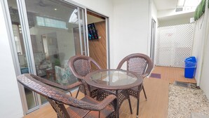 A patio area with wicker furniture, a glass table, and a blue trash bin.