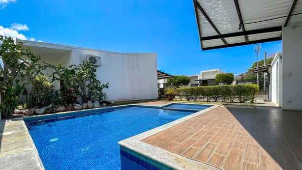 A swimming pool with clear blue tiles, surrounded by a wooden deck and a white building.