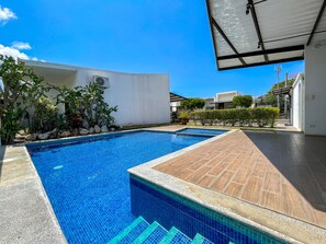 A swimming pool with clear blue tiles, surrounded by a wooden deck and a white building. - Charming Jaco Beach Condo Vereda B3 (Jacó)