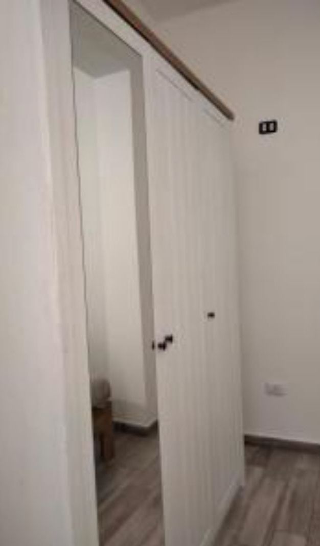 A room with a white door, a small stool, and a light switch on the wall.