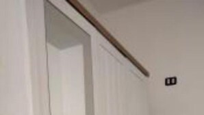 A room with a white door, a small stool, and a light switch on the wall. - CASA AI TRE CAMPANILI - Apartment 2 (Gela)