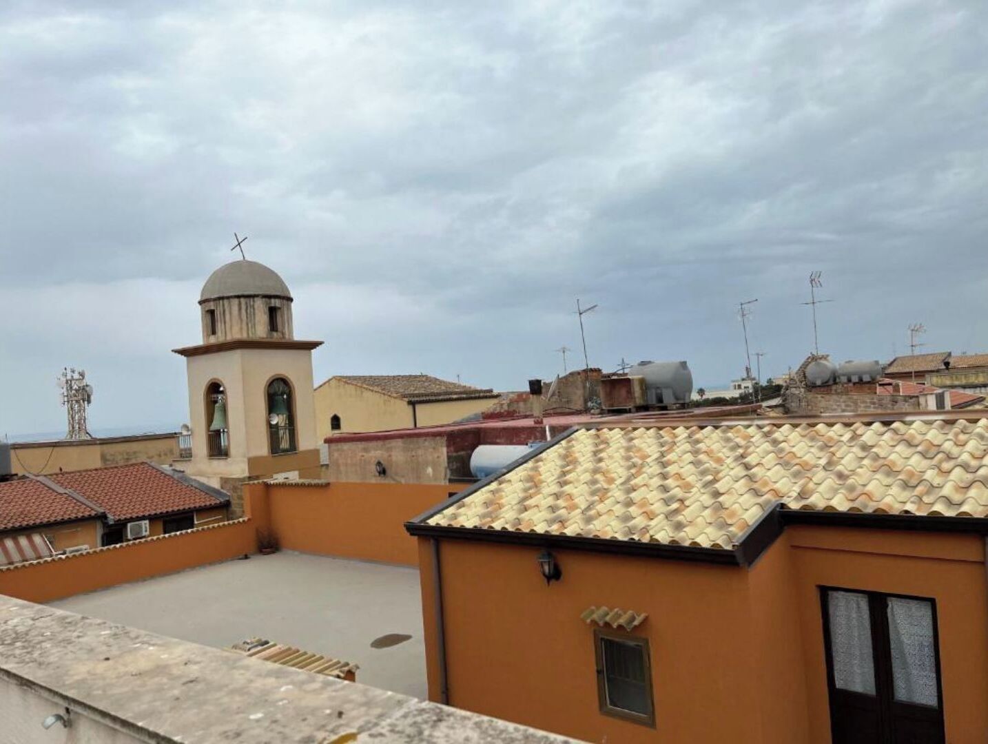 A rooftop with terracotta tiles, a bell tower, and a clear sky.