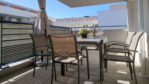 Ein Balkon mit Tisch, Stühlen, einer Topfpflanze und einer Weinflasche.