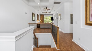 A spacious hallway with a wooden staircase, white walls, and a ceiling fan.