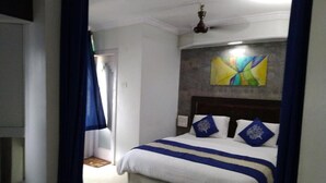 Un dormitorio con una cama, un ventilador de techo y un cuadro abstracto de colores en la pared.