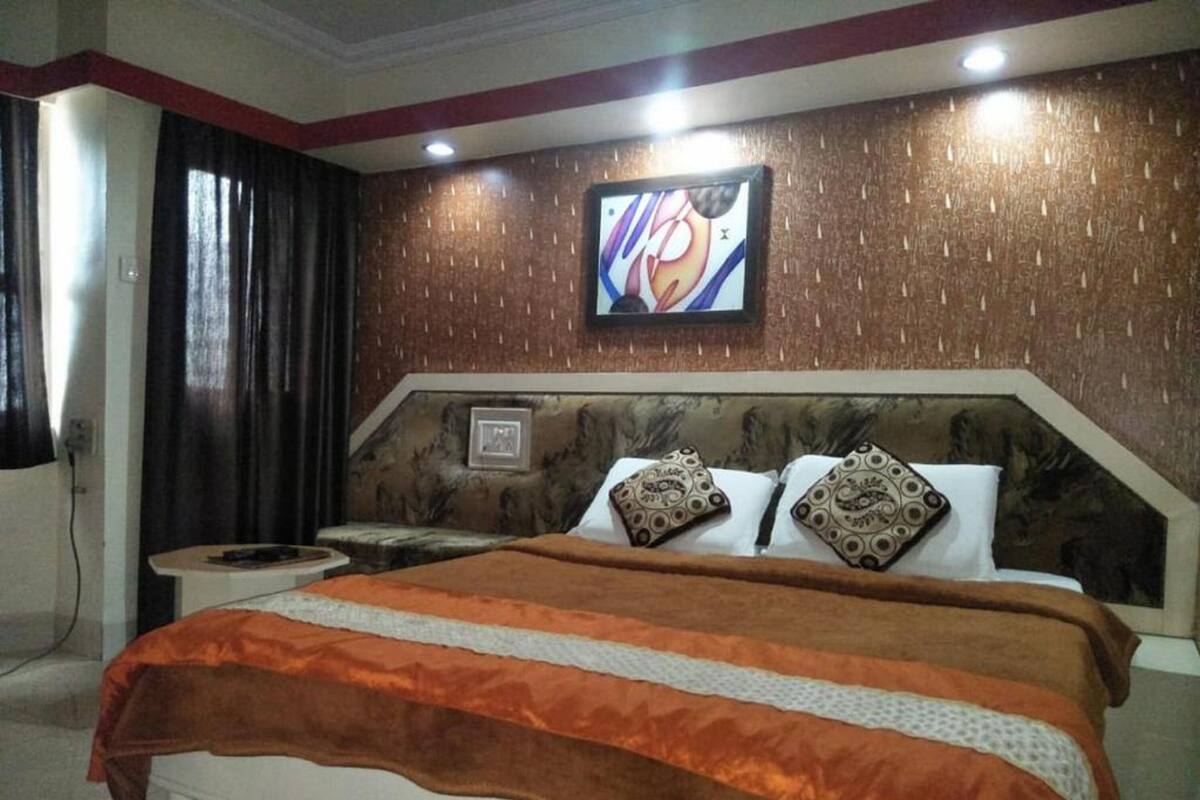 Un dormitorio con una cama grande, una mesita de noche, un televisor montado en la pared y un cuadro.