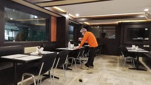Un restaurante con mesas y sillas, una persona atendiendo y un amplio ventanal.