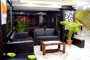 Un hall d’entrée avec des canapés en cuir noir, une table basse en bois et des plantes en pot.