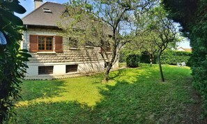 A stone house with a sloped roof, wooden shutters, and a small garden with a lawn and trees. - Villa with large garden in quiet location near Paris, Orly, forest and lakes (Draveil)