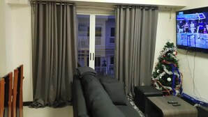 Un salon avec un canapé gris, une petite télévision et un sapin de Noël décoré.