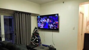 Un salon avec un téléviseur fixé au mur, un petit sapin de Noël et un canapé.