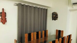 Un coin repas avec une table en verre et des chaises en bois, un rideau gris et deux masques décoratifs fixés au mur.