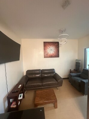 A living room with a brown leather sofa, a wooden coffee table, a flat-screen TV, and a modern pendant light.