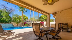 Eine überdachte Terrasse mit Pool, Gartenmöbeln und einer Pergola mit hängenden Lichtern.