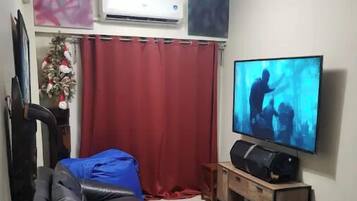 A living room with a black leather sofa, a red curtain, a television, and an air conditioning unit.