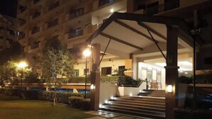 A well-lit outdoor area with a covered entrance, steps leading to a building, and a small garden with a tree and shrubs. - Mucucu's place (Pasig)