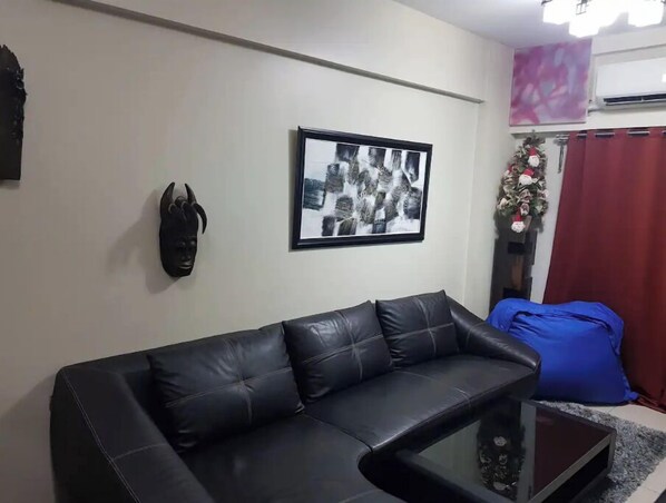 A living room with a black leather sofa, a framed black and white photograph, and a decorative mask on the wall.