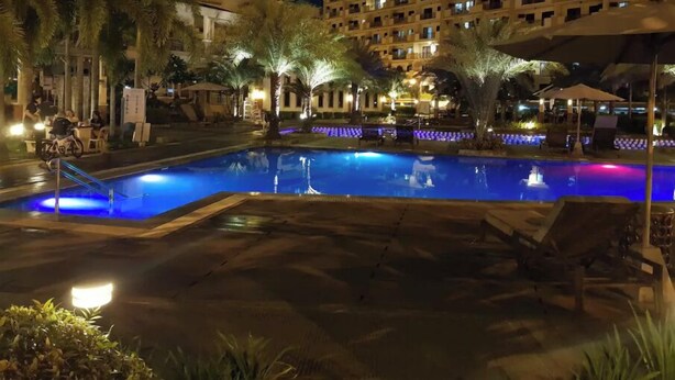 A nighttime pool area with palm trees and a building in the background. - Mucucu's place (Pasig)