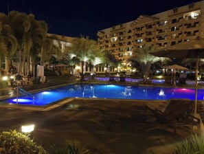 A nighttime pool area with palm trees and a building in the background.