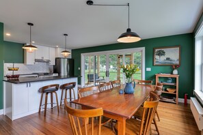 A modern kitchen with white cabinets, a wooden dining table, and pendant lighting. - Step-free lake house, screened porch (Dedham)