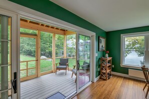 A room with a sliding glass door leading to a deck, a chair, and a small table with a vase. - Step-free lake house, screened porch (Dedham)