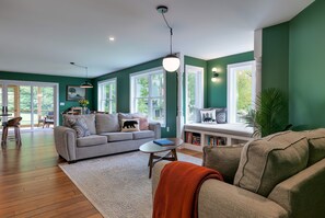 A spacious living room with a large sofa, a coffee table, and a window seat with books. - Step-free lake house, screened porch (Dedham)