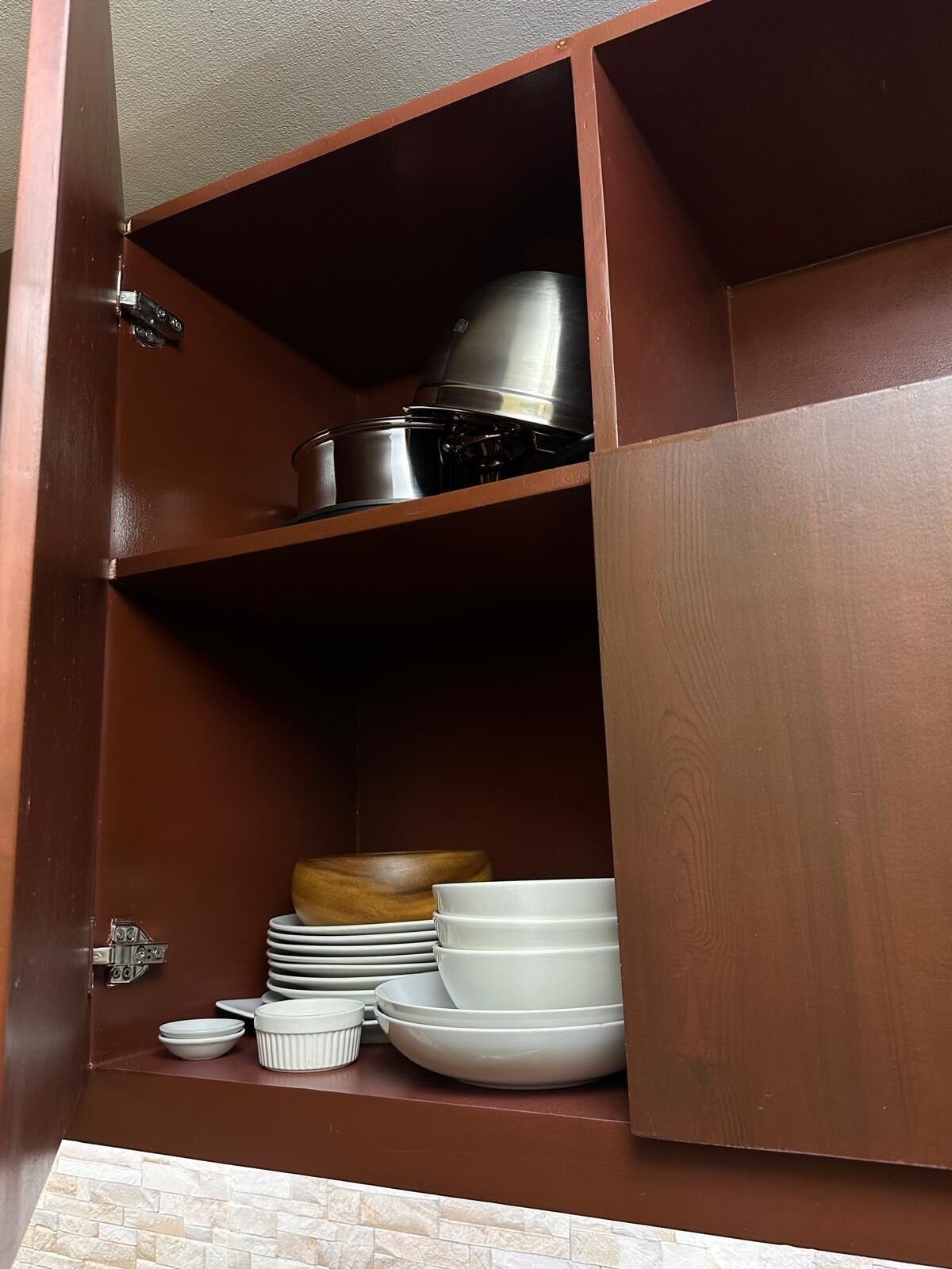 A wooden cabinet with shelves containing kitchenware, including plates, bowls, and a pot.