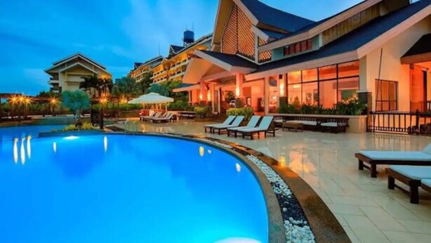 A hotel with a swimming pool, lounge chairs, and a traditional architectural style. - Central place  (Malay)