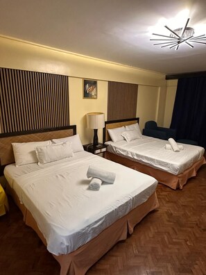 A hotel room with two beds, a nightstand, a lamp, and a ceiling light fixture.