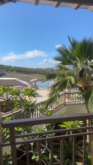 Un balcón con vista a una playa, palmeras y una piscina.