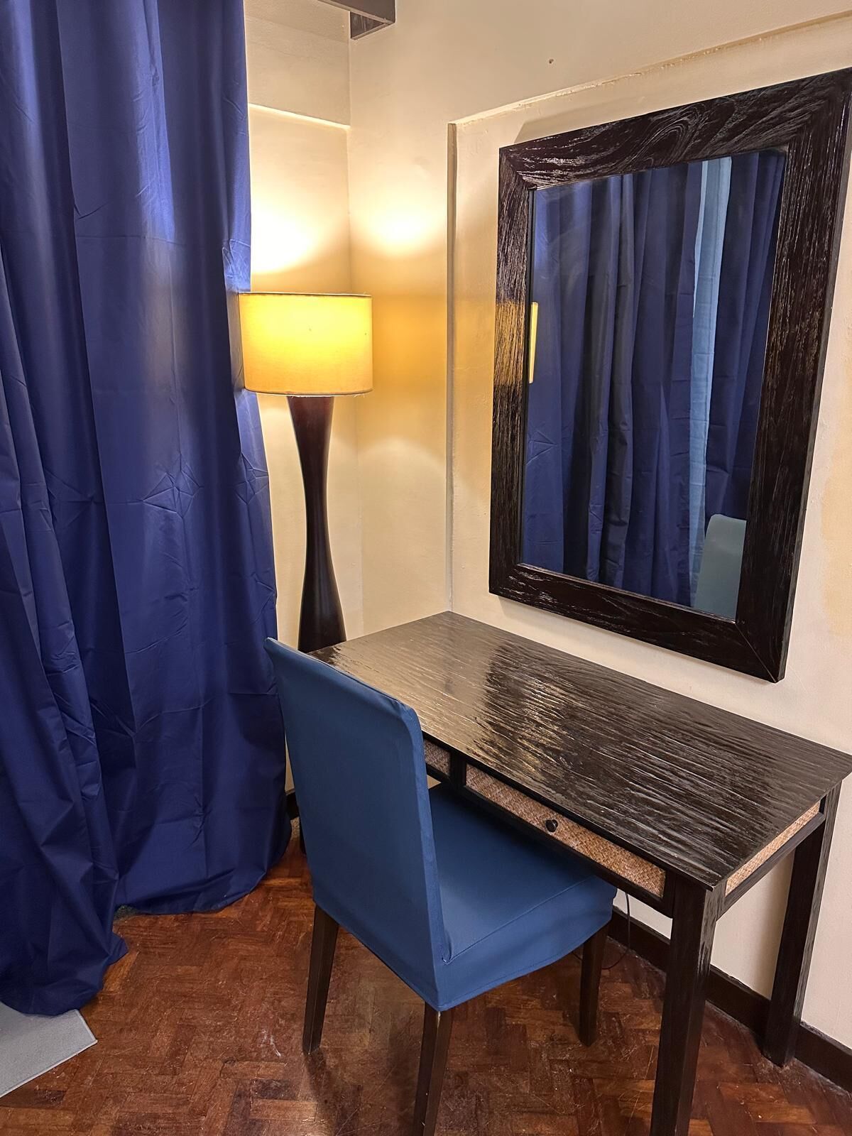 Ett rum med ett skrivbord, en stol, en lampa och en stor spegel på väggen.