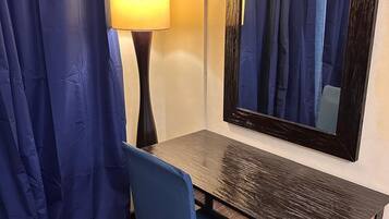 Ett rum med ett skrivbord, en stol, en lampa och en stor spegel på väggen.