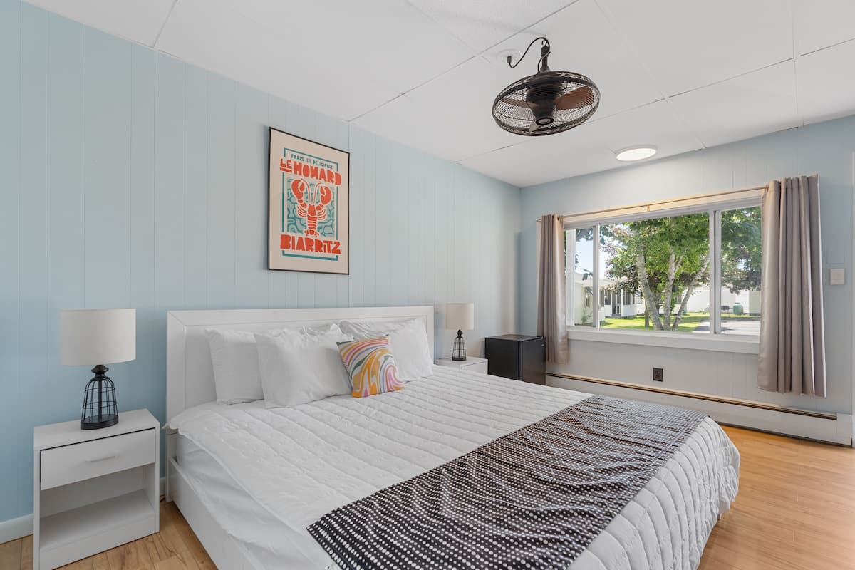 A bedroom with a bed, nightstands, a window with curtains, and a wall-mounted fan.