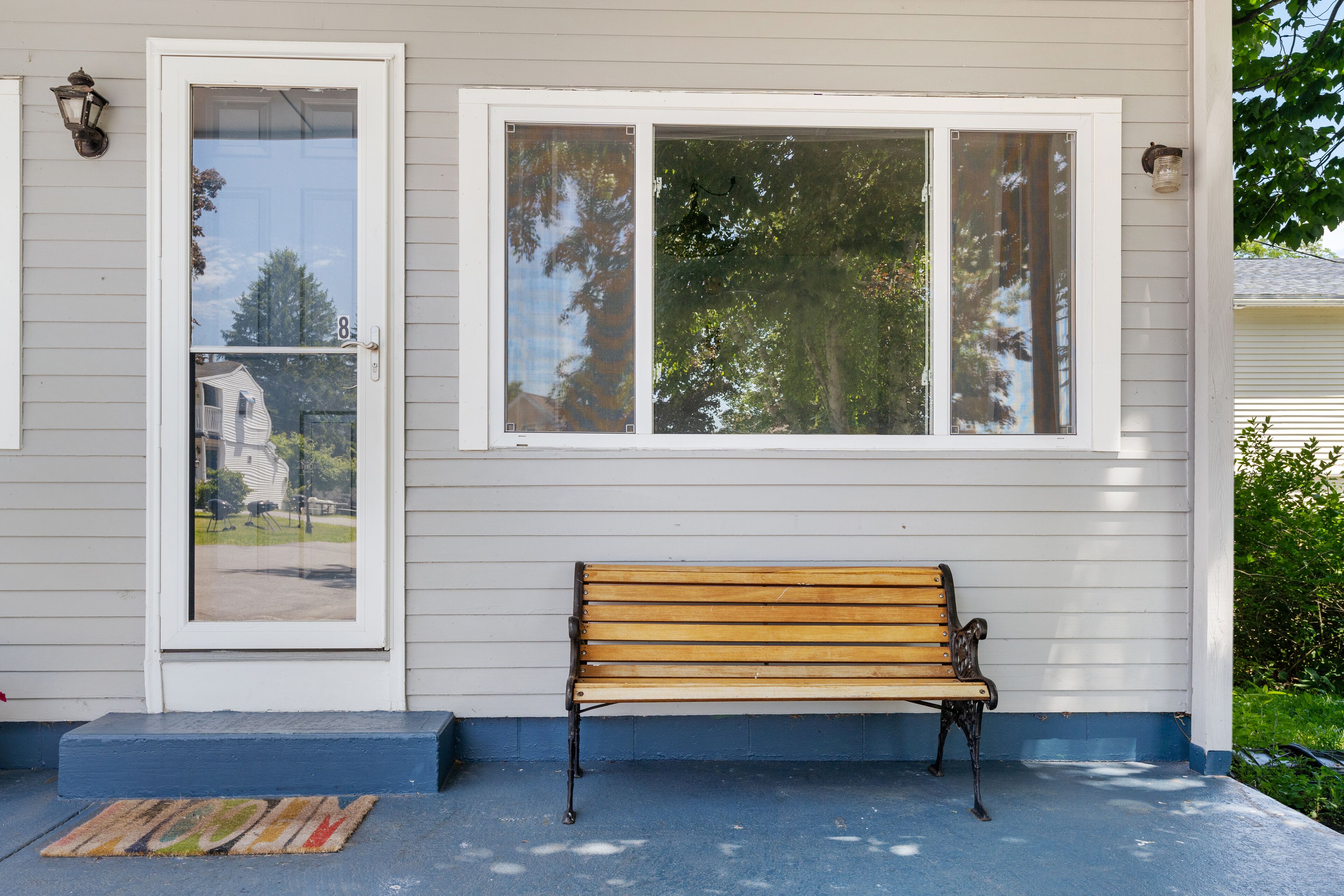 A wooden bench outside a house with a white door and windows.