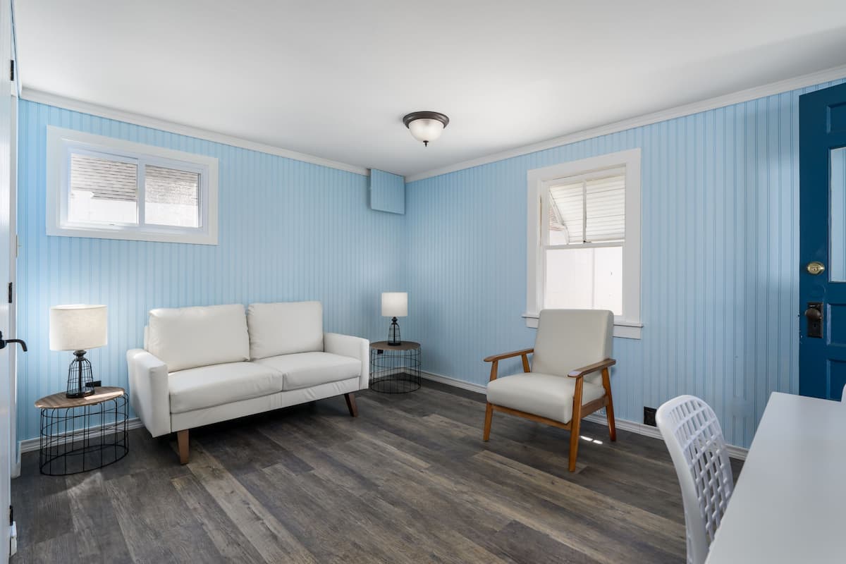 A room with blue walls, a white sofa, a wooden chair, and a dining table.