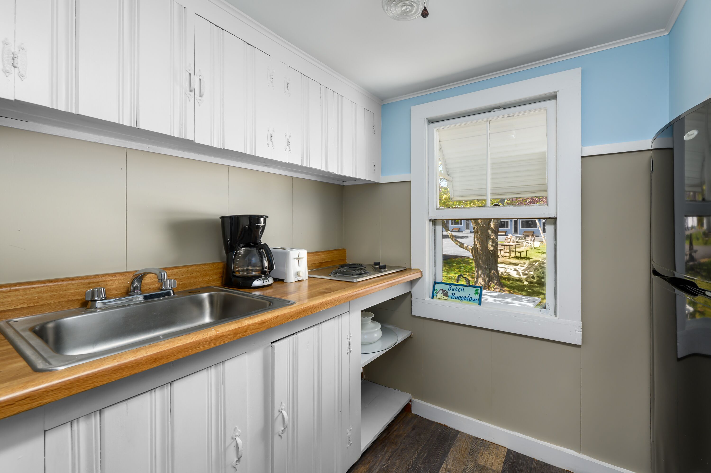 A kitchen with white cabinets, a wooden countertop, a sink, a coffee maker, and a window with a view of the outdoors.