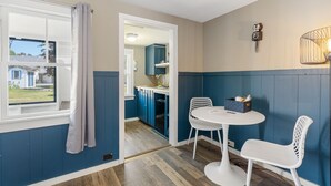 A room with a window, a table with two chairs, and a view into the kitchen.