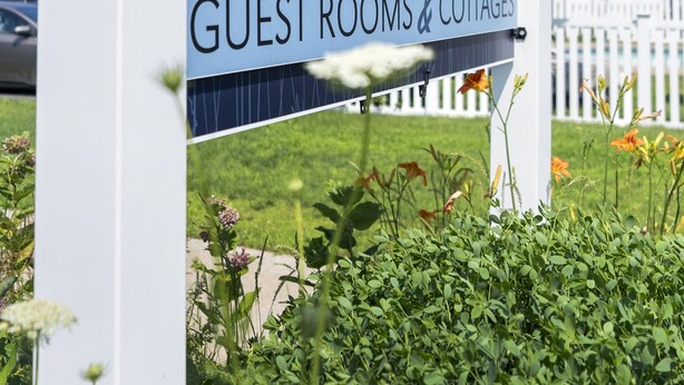 A sign for "The Beaches" guest rooms and cottages with a clear sky and a white fence in the background.