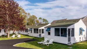 A row of white mobile homes with blue awnings, a paved driveway, and a grassy area with lounge chairs.